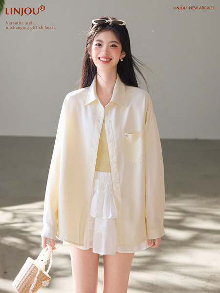 Young woman wearing a light cream oversized shirt with a white outfit and woven handbag