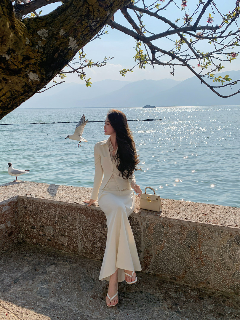 Woman wearing a cream elegant outfit by the seaside with a matching handbag