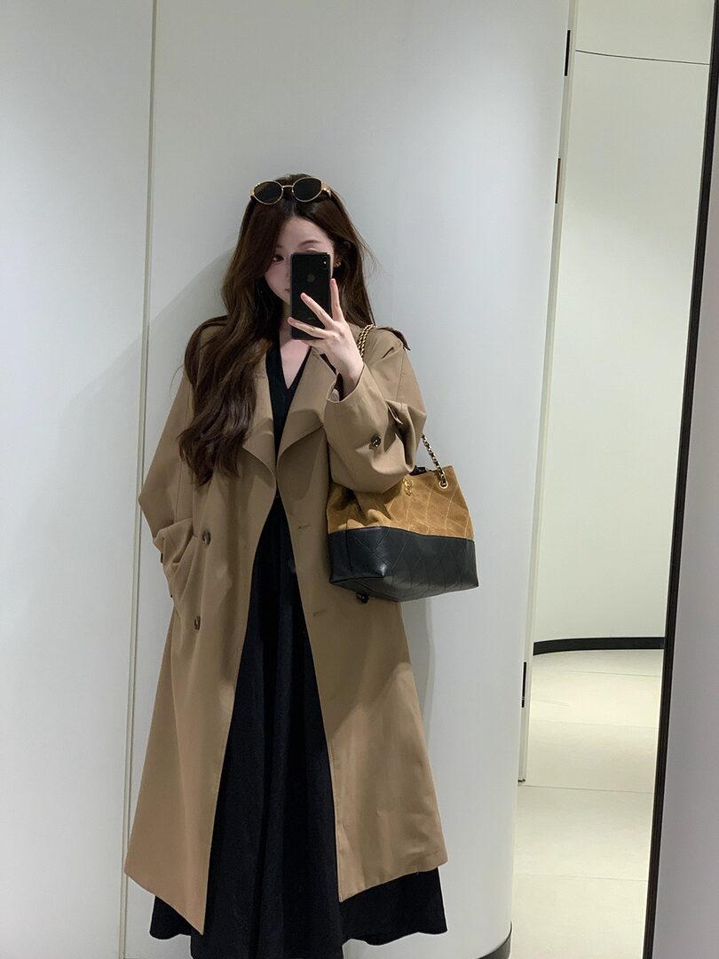 Woman wearing a beige trench coat and carrying a two-tone handbag in a mirror selfie
