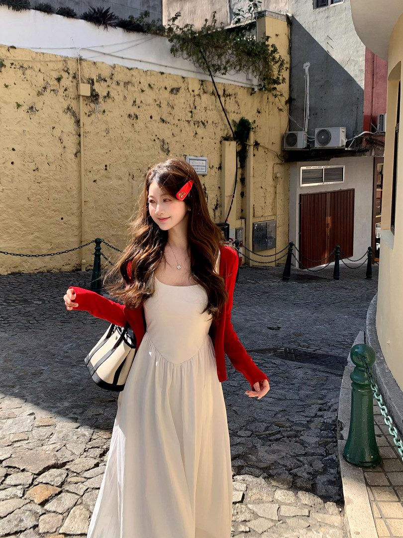 Woman wearing a white maxi dress with a red cardigan and handbag outdoors