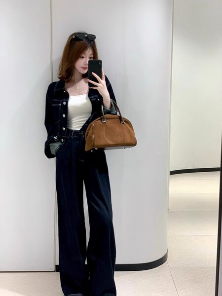 Woman wearing a dark denim outfit and holding a brown handbag in a mirror selfie