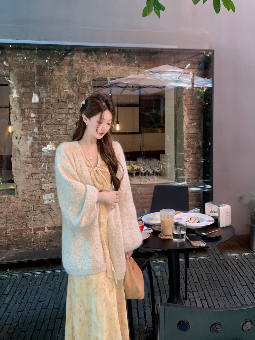 Woman wearing a light cream cardigan over a pale yellow dress in a cafe