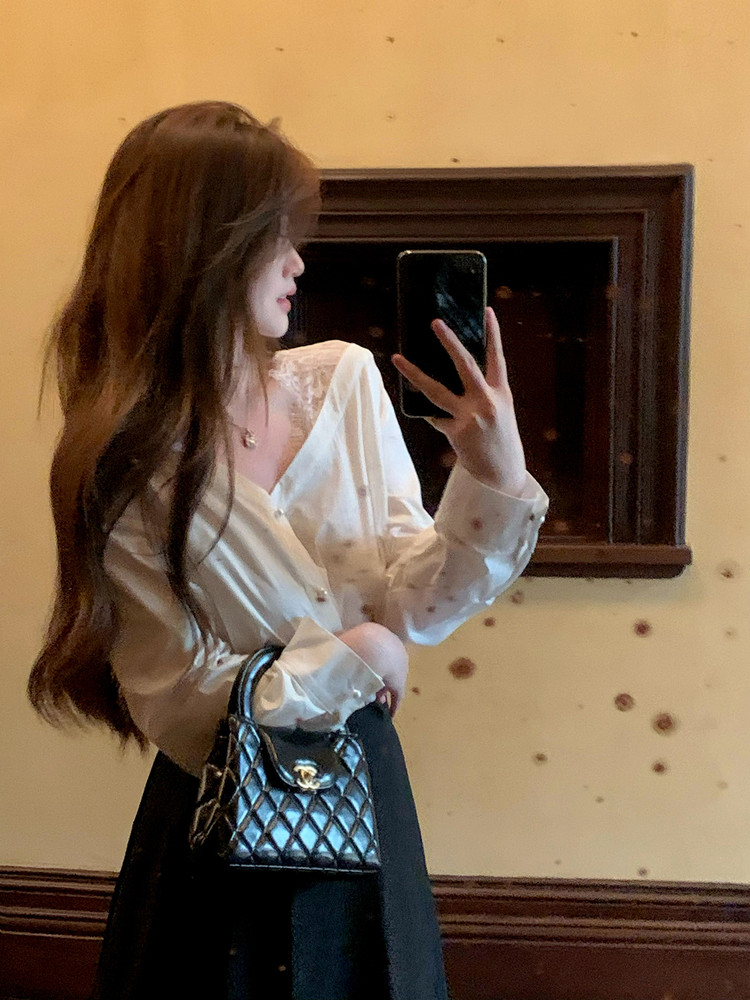 Woman wearing a white blouse and black skirt, holding a black quilted handbag in a mirror selfie