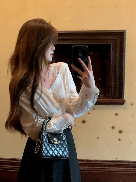Woman wearing a white blouse and black skirt, holding a black quilted handbag in a mirror selfie