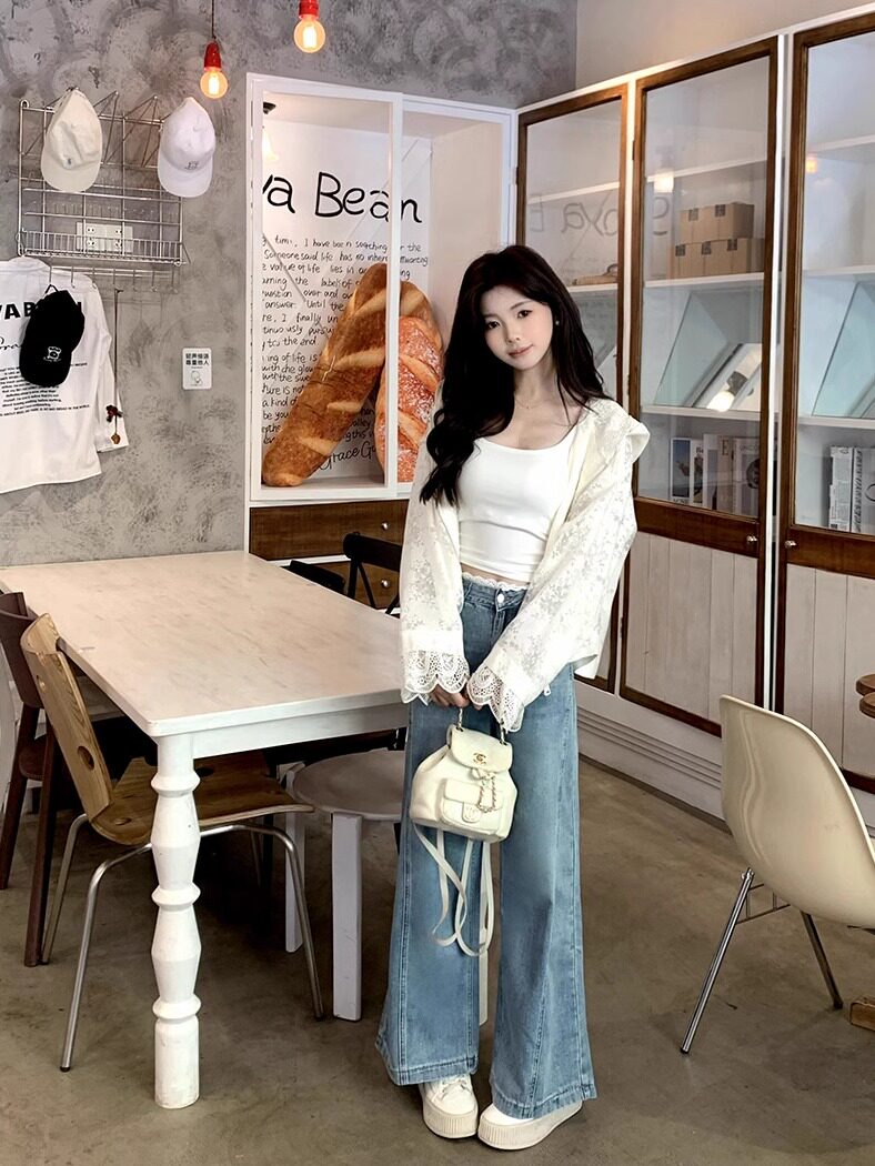 Model wearing a white lace cardigan, white tank top, wide-leg jeans, and a small cream backpack