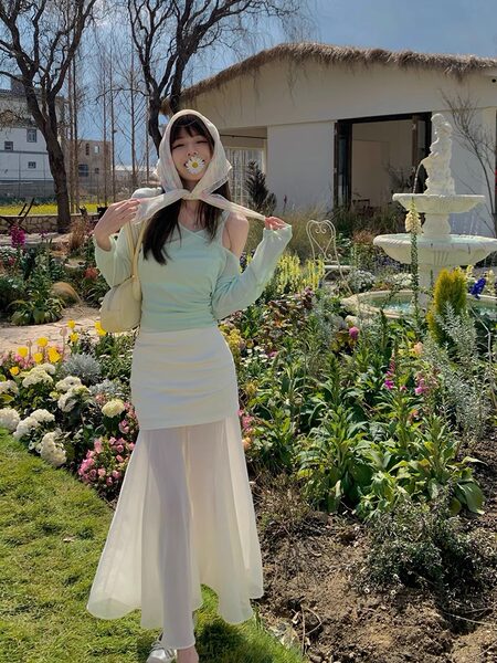 Woman wearing a pastel green top with a white sheer maxi skirt in a garden