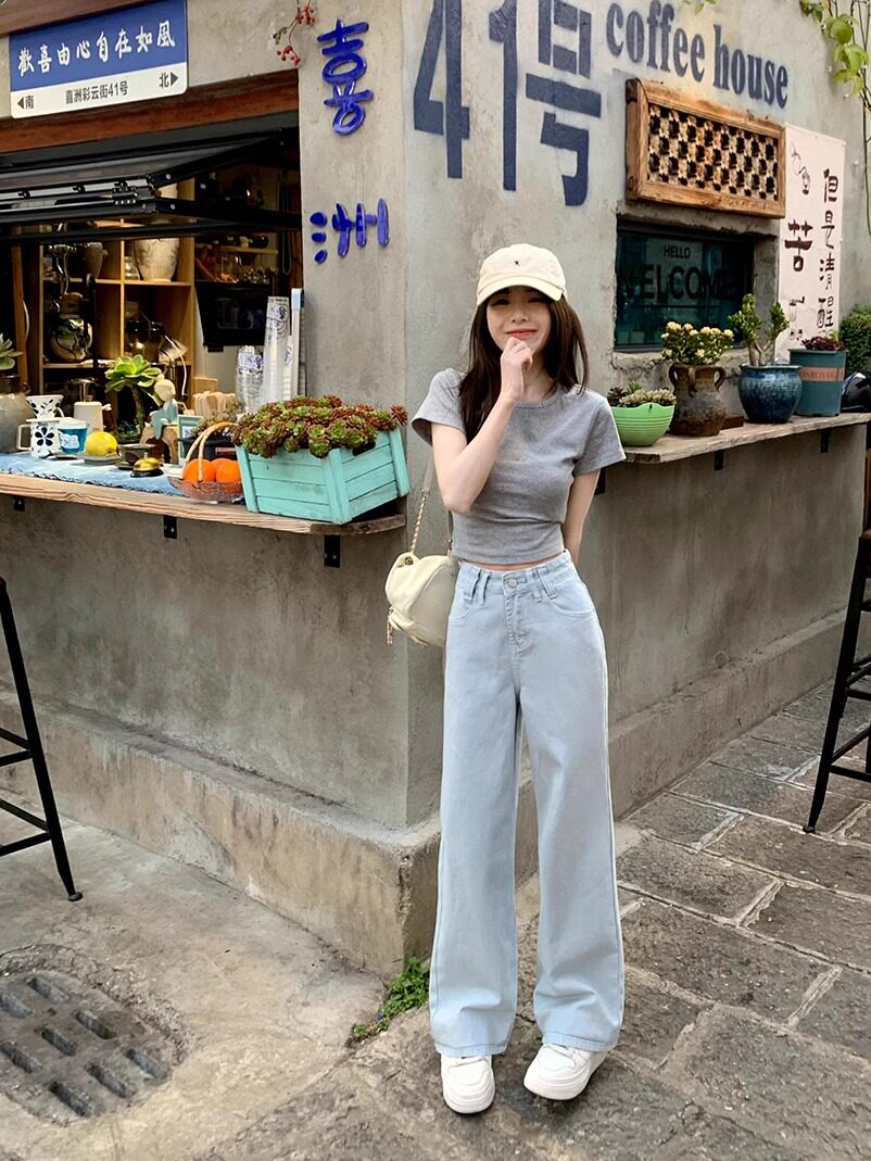 Woman wearing a gray fitted T-shirt and light blue wide-leg jeans with a cap and shoulder bag