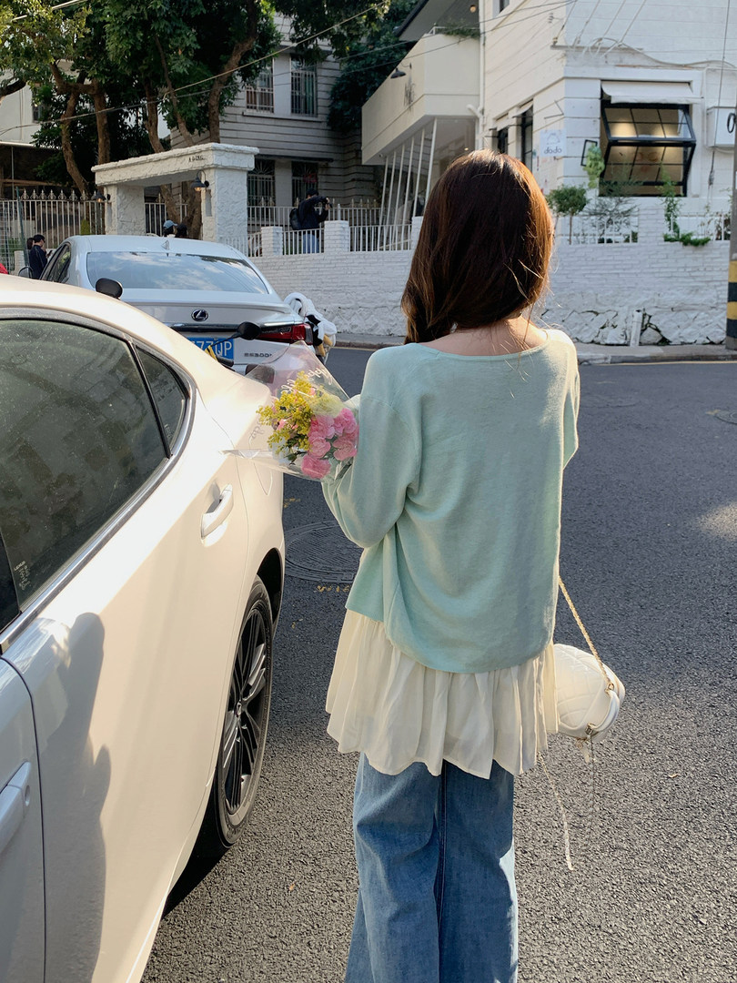 Woman wearing a mint sweater over a white layered shirt with jeans outdoors
