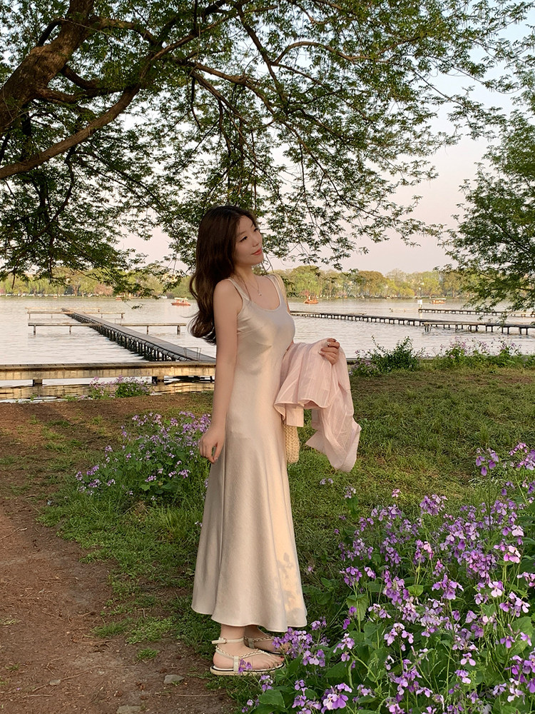 Woman wearing a long beige satin slip dress outdoors by a lakeside