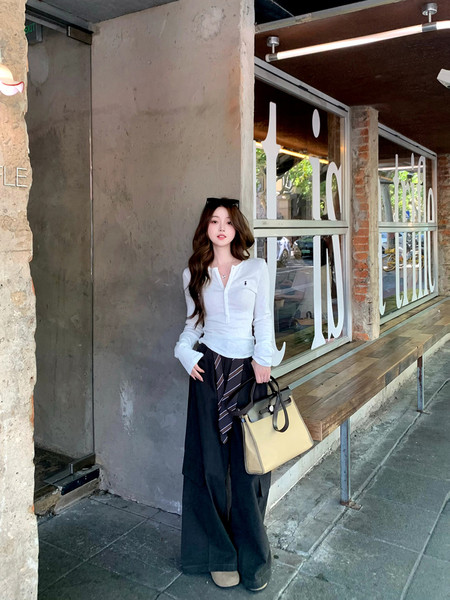 Woman wearing a white blouse with black wide-leg pants and a beige handbag