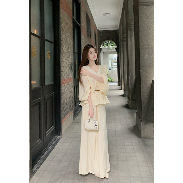 Model wearing a cream long-sleeve flowing dress with a small handbag