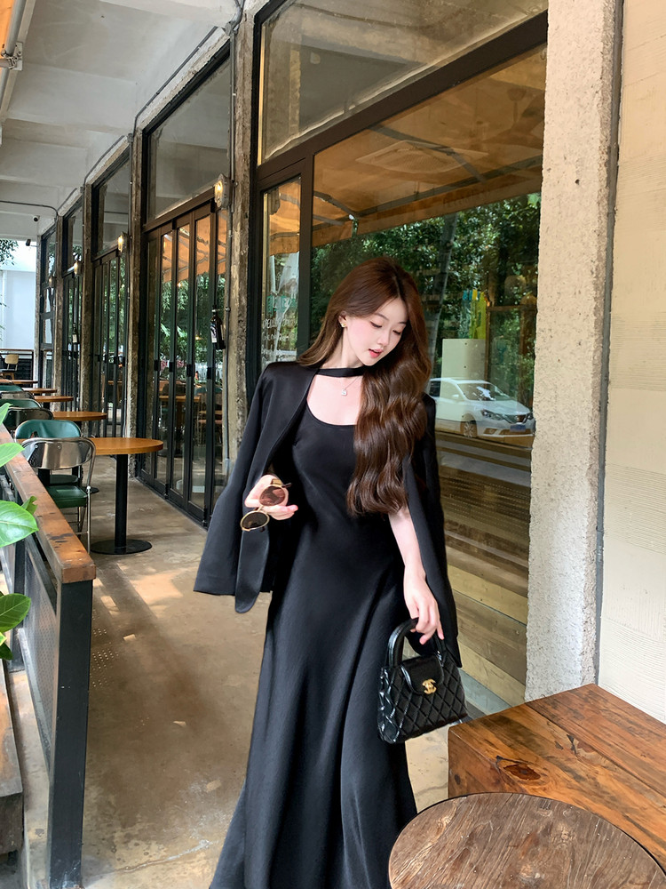 Woman wearing a black elegant long dress with a matching cape jacket and small quilted handbag