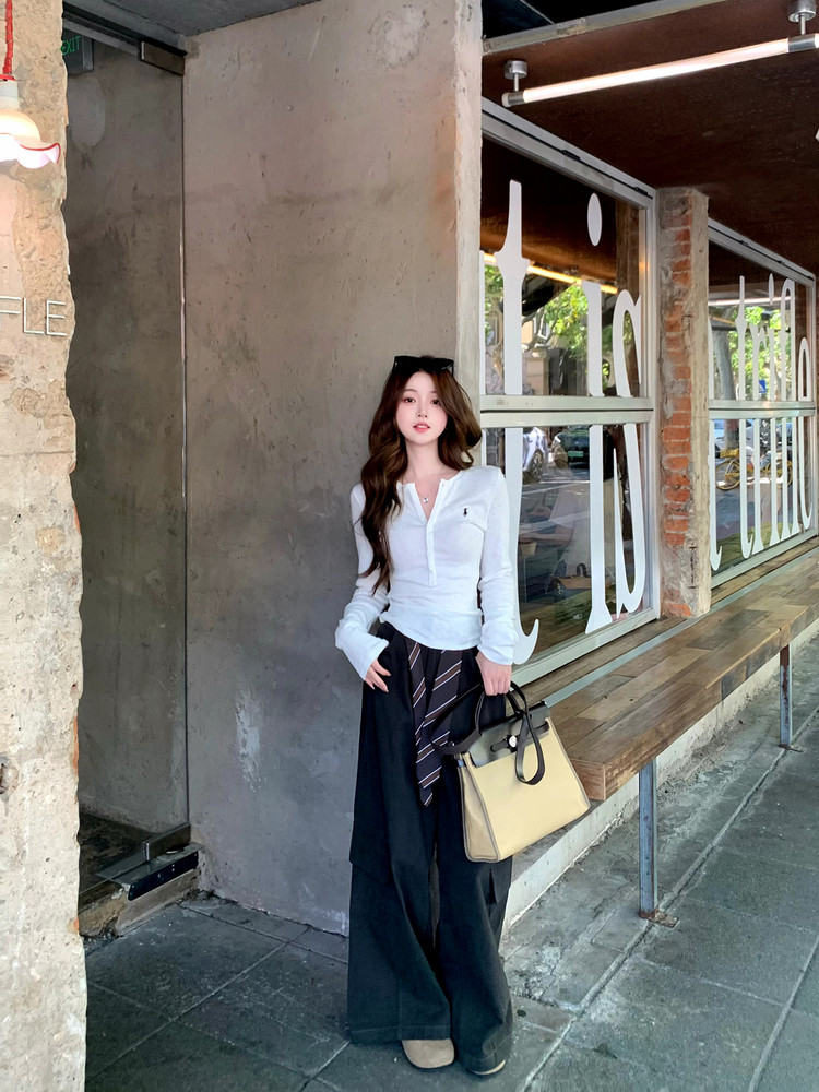 Woman wearing a white long-sleeve top with wide-leg black pants and carrying a beige handbag