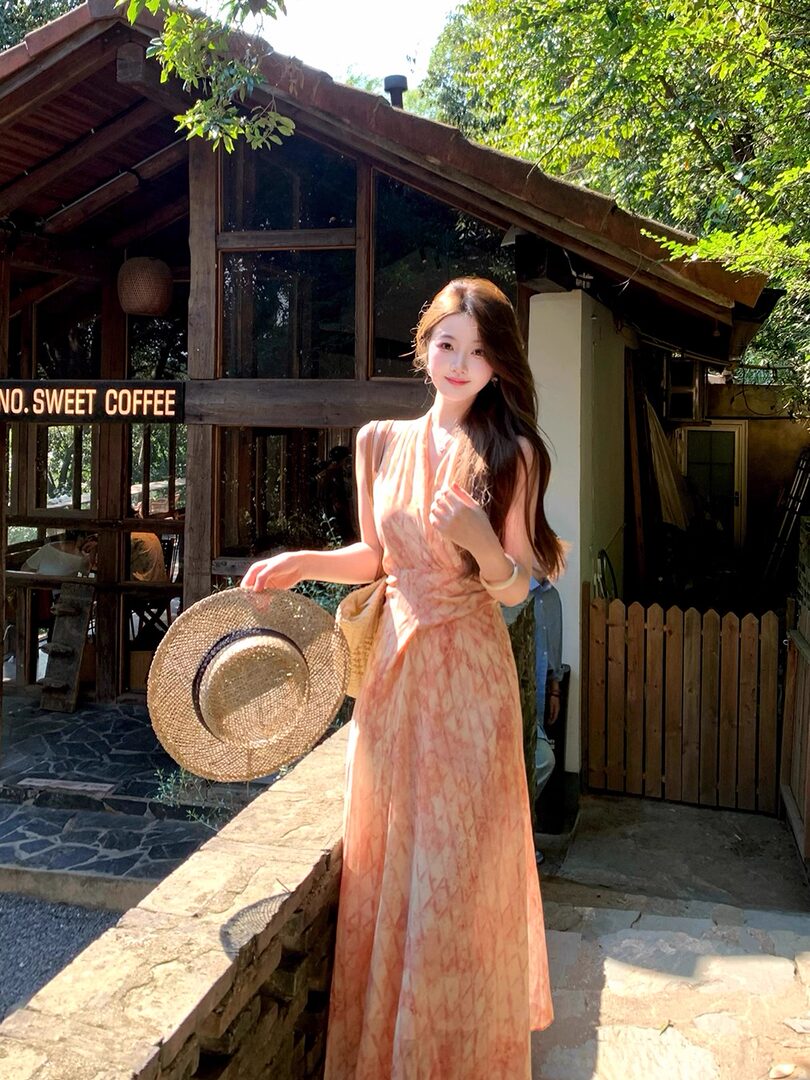 Woman wearing a peach sleeveless maxi dress outdoors with a straw hat