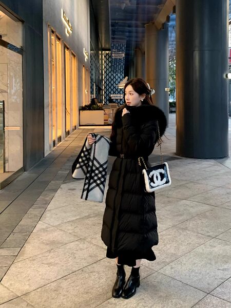 Woman wearing a long black padded winter coat with fur collar and a small chain handbag