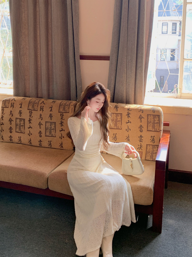 Woman wearing a white long-sleeve dress while seated on a sofa