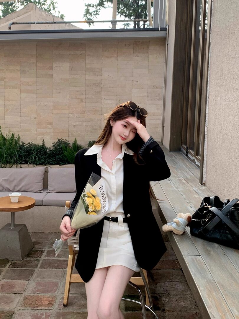 Woman wearing a black blazer over a white blouse and skirt, holding flowers outdoors