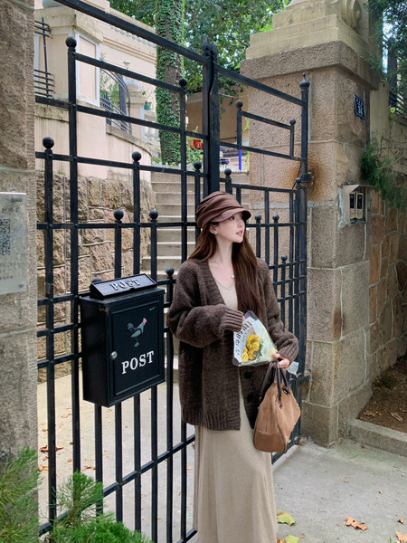 Woman wearing a brown cardigan and beige dress with a brown hat and handbag