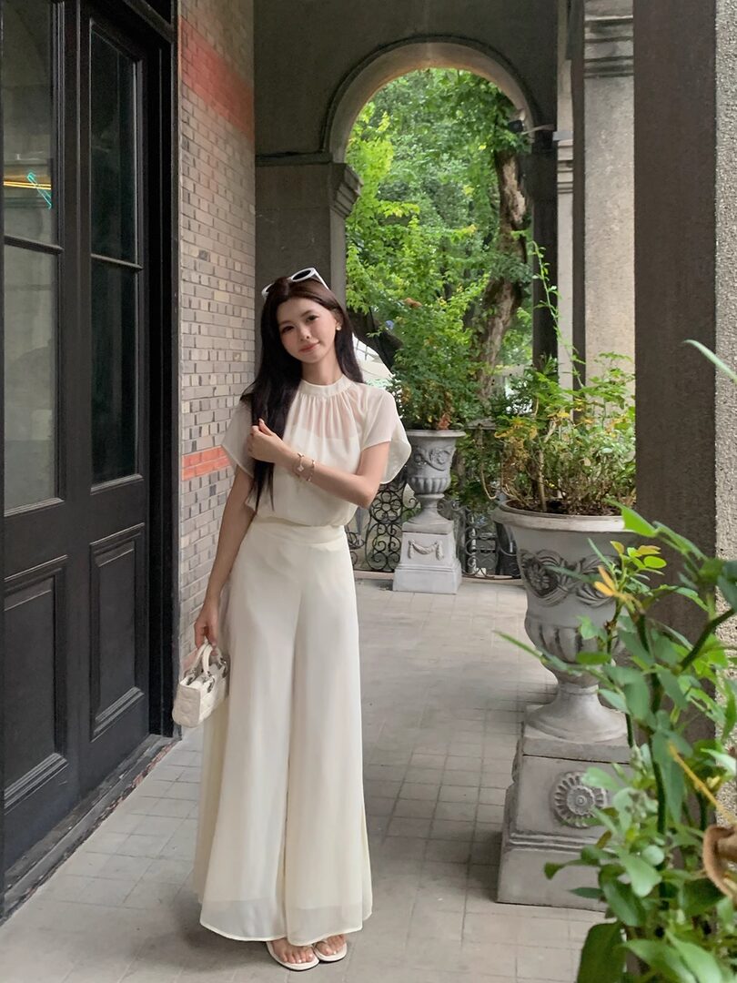 Woman wearing a cream wide-leg outfit with a sheer short-sleeve top outdoors