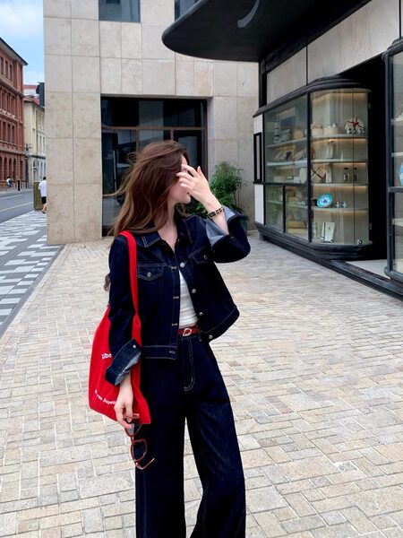 Woman wearing a dark denim jacket and matching jeans with a red tote bag