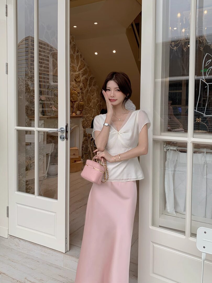 Woman wearing a white blouse and pink long skirt holding a pink handbag