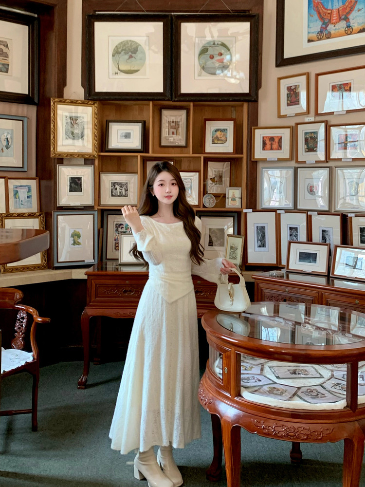 Woman wearing a long white dress and holding a white handbag indoors