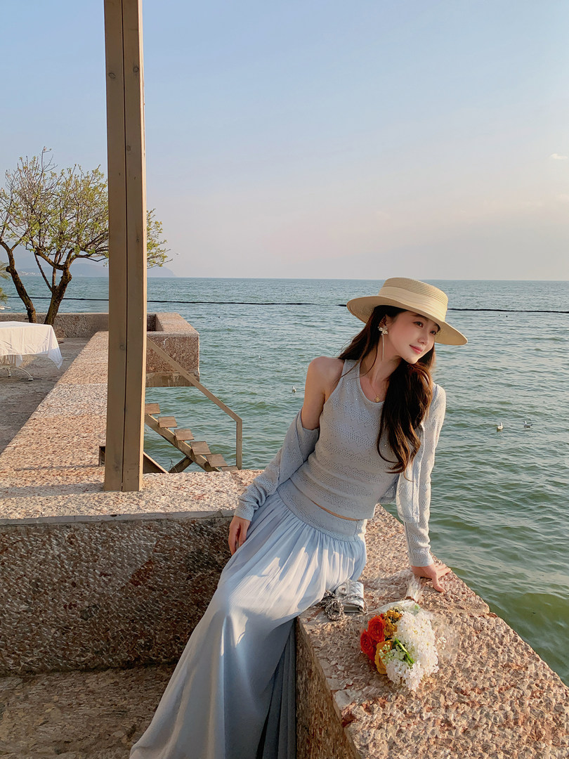 Woman modeling a light blue beach outfit with a wide-brim hat by the sea