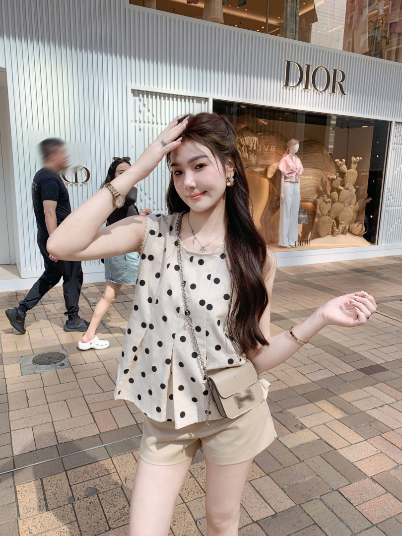 Woman modeling a beige polka dot sleeveless top with matching shorts and a small crossbody bag outdoors