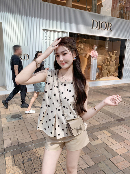 Woman modeling a beige polka dot sleeveless top with matching shorts and a small crossbody bag outdoors
