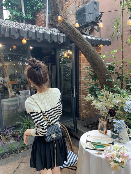 Woman wearing a striped knit sweater and pleated skirt with a black quilted chain bag