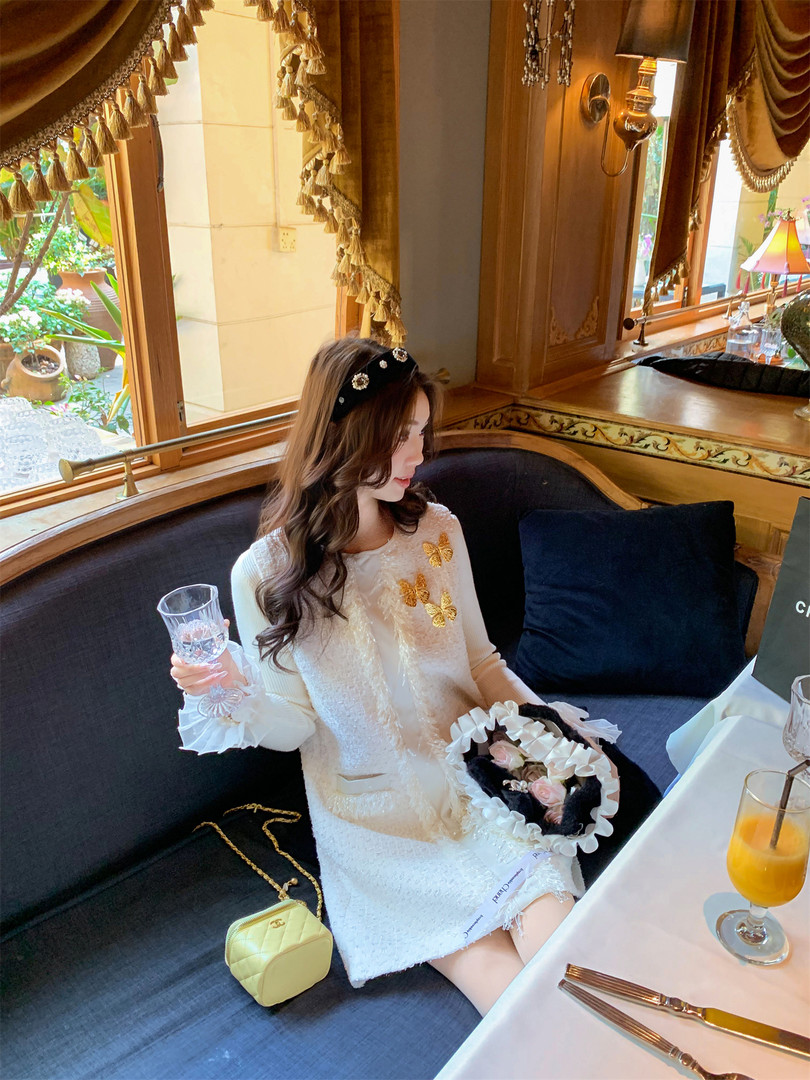 Woman wearing a white textured mini dress with butterfly embellishments in a restaurant setting