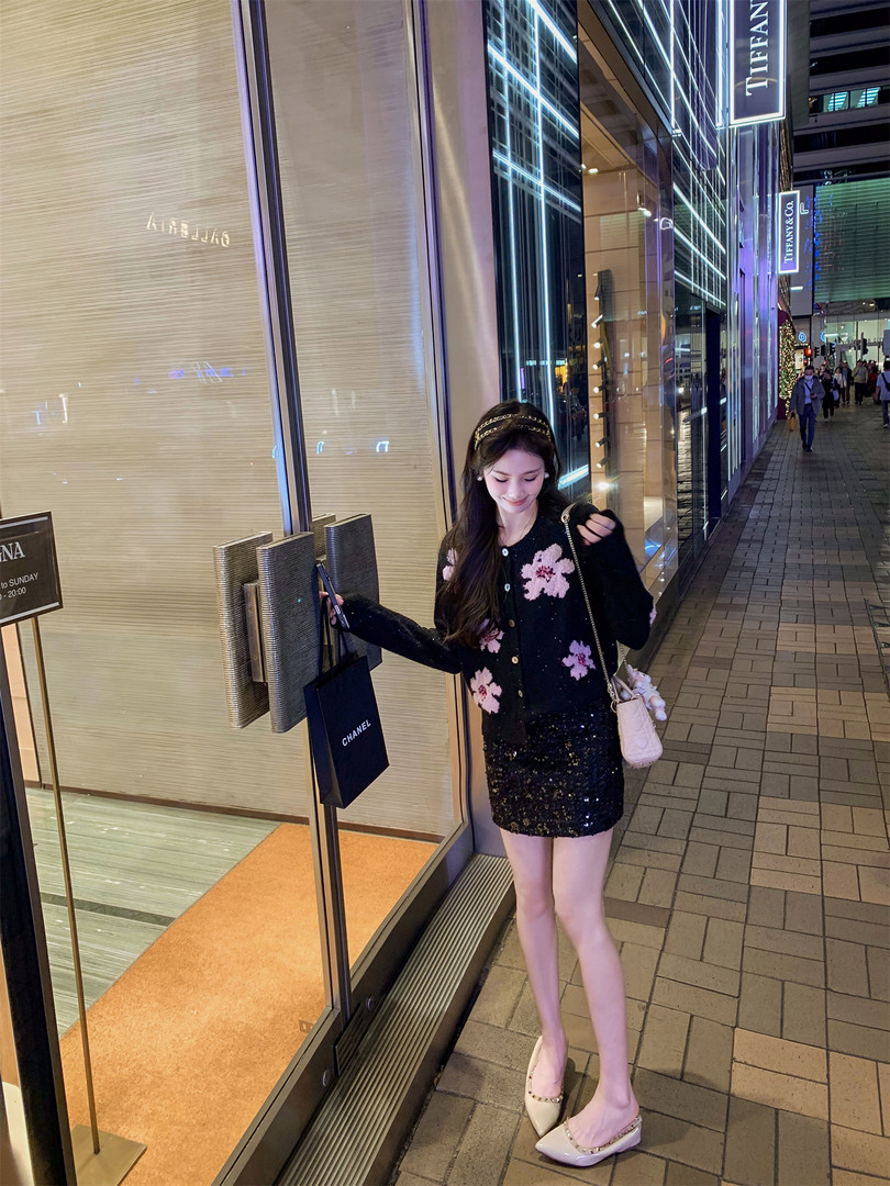 Woman wearing a black floral cardigan with a sequined skirt and cream slingback flats outside a luxury store