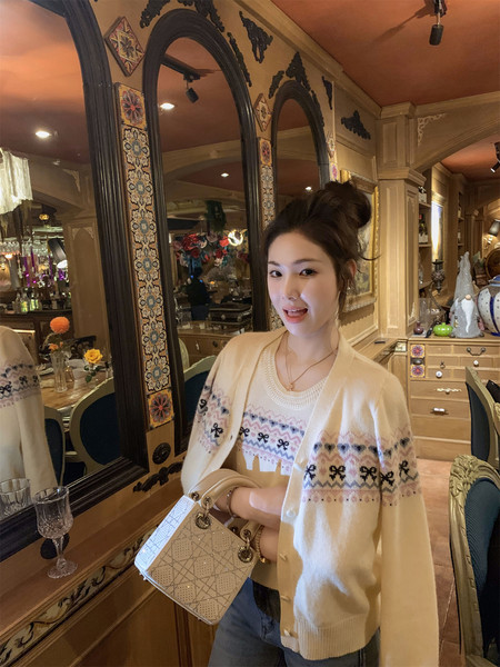 Woman wearing a cream patterned cardigan and holding a white handbag