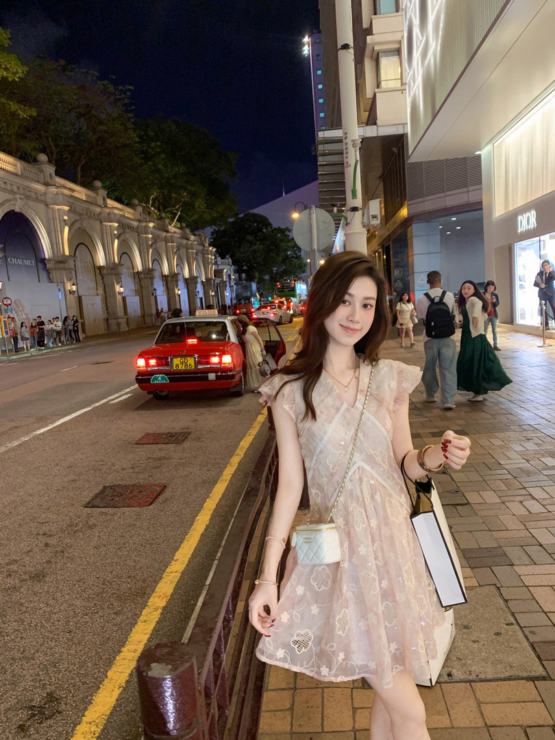 Woman wearing a light pink sheer embroidered dress on a city street at night