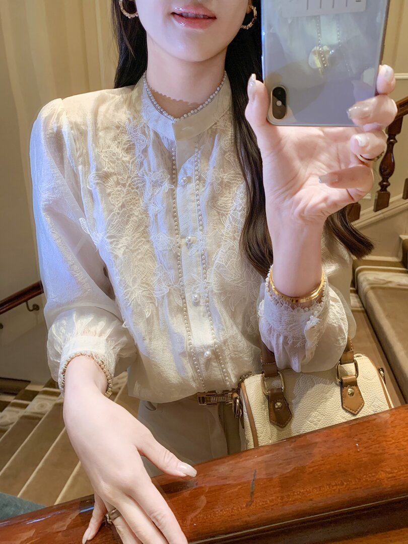 Woman wearing a sheer white embroidered blouse with pearls and carrying a beige handbag