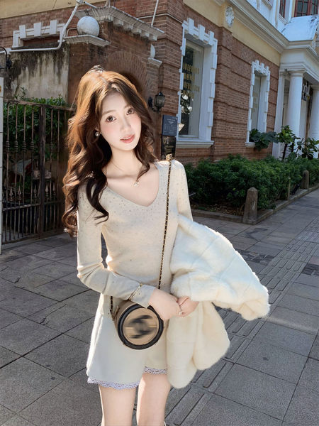Woman wearing a cream knit dress with a white faux fur coat and round crossbody bag outdoors