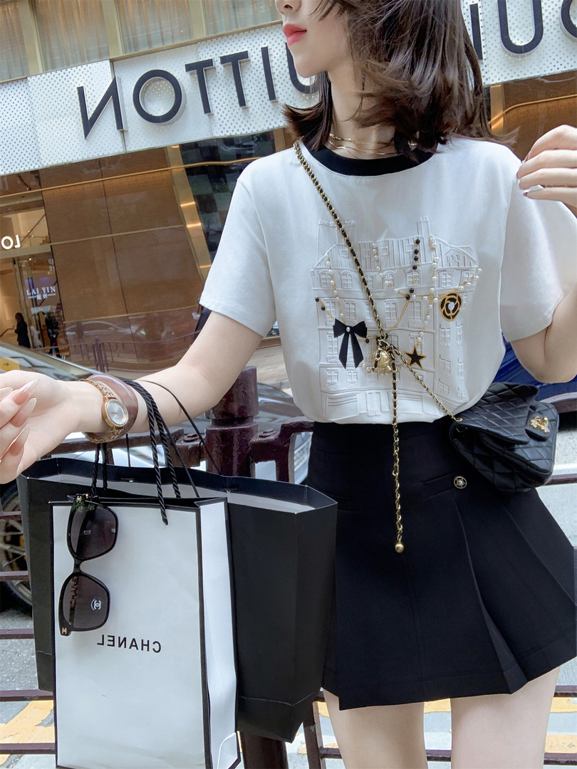 Woman wearing a white embellished T-shirt and black skirt with chain accessories, shown as a fashion outfit.