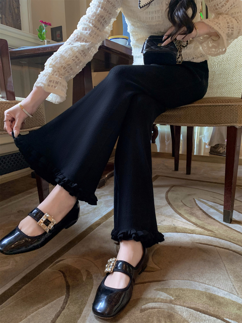 Model wearing black wide-leg pants with ruffled hems and black buckle flats