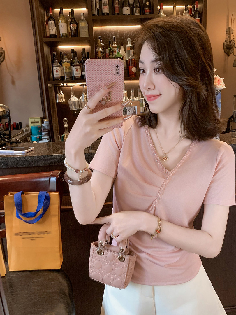 Woman wearing a pink V-neck top holding a small pink quilted handbag.