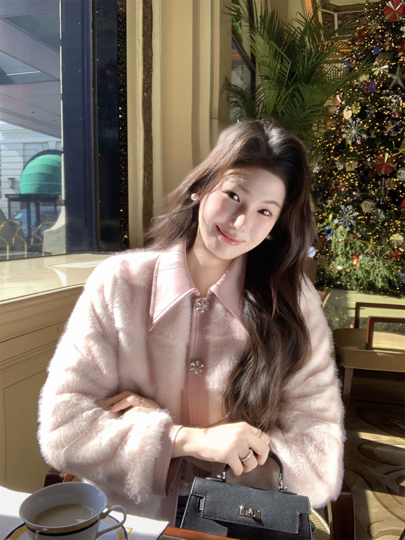 Woman wearing a light pink fuzzy coat and holding a black handbag