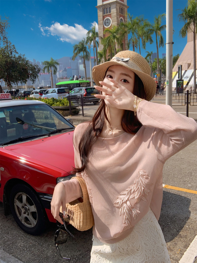 Woman wearing a pink long-sleeve top, white lace skirt, straw hat, and woven bag outdoors