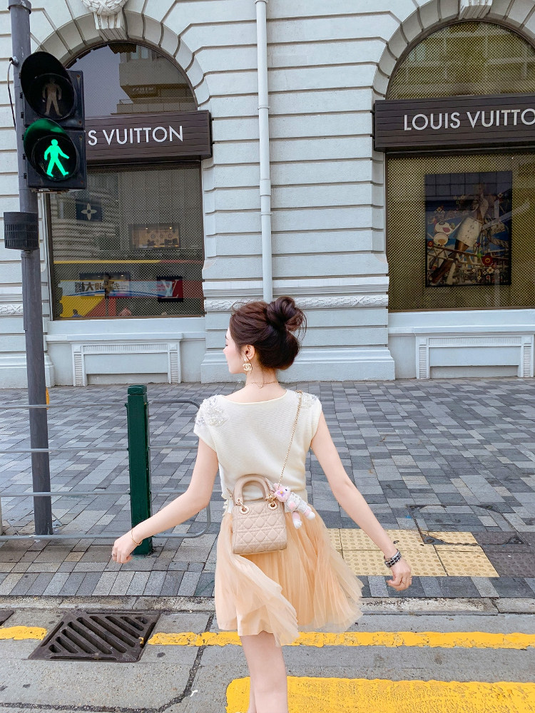 Woman wearing a light cream top and peach tulle skirt with a small quilted handbag on a city street