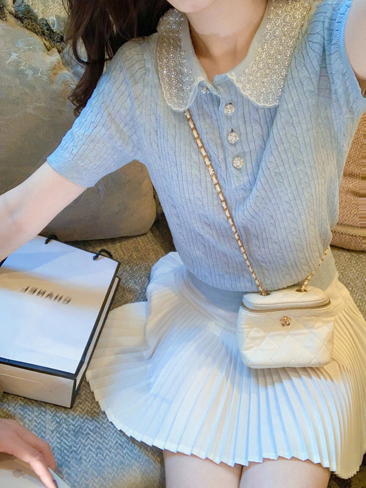 Woman wearing a light blue knit top with a white pleated skirt and small quilted crossbody bag
