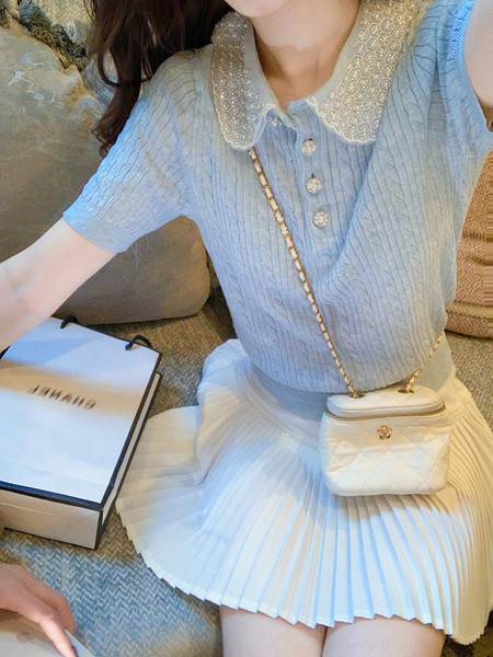 Woman wearing a light blue knit top with a white pleated skirt and small quilted crossbody bag