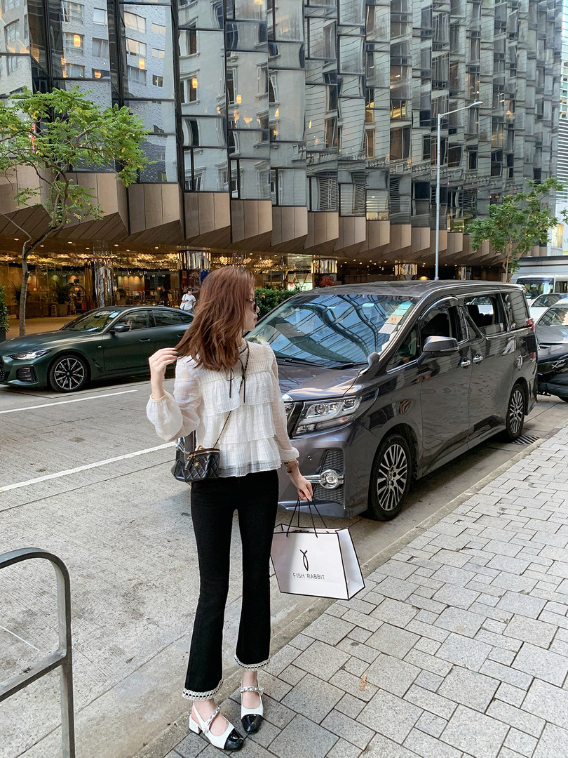 Woman wearing a white ruffled blouse, black pants, and two-tone heels on a city street