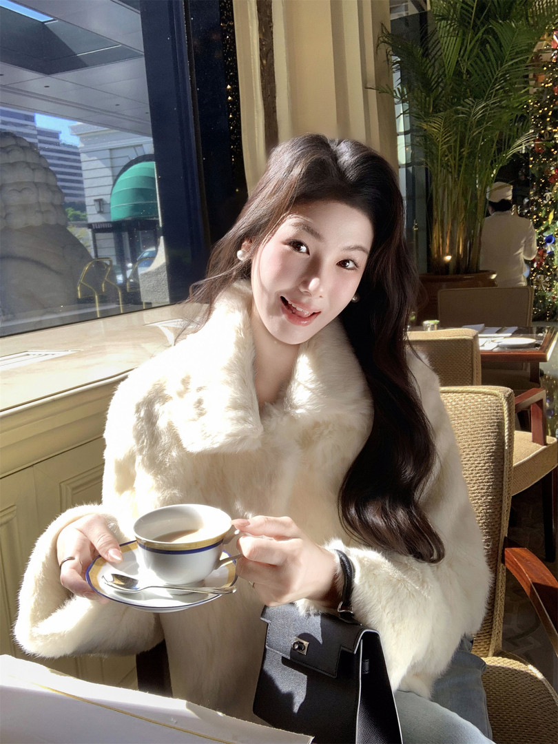 Woman wearing a white fur coat and holding a black handbag in a restaurant