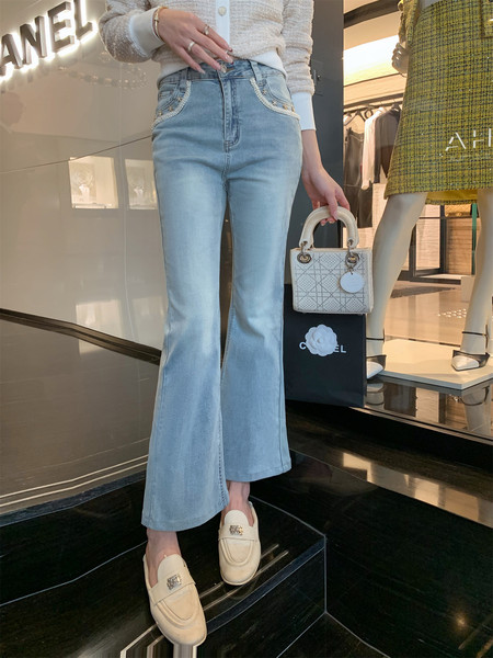Model wearing light blue flared jeans with embellished pockets, cream loafers, and holding a small white handbag
