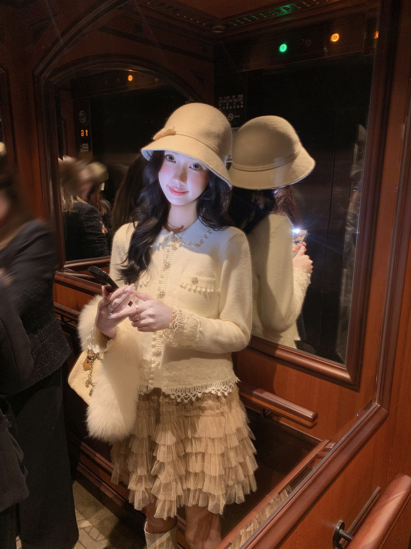 Model wearing a cream outfit with a matching cloche hat and layered skirt