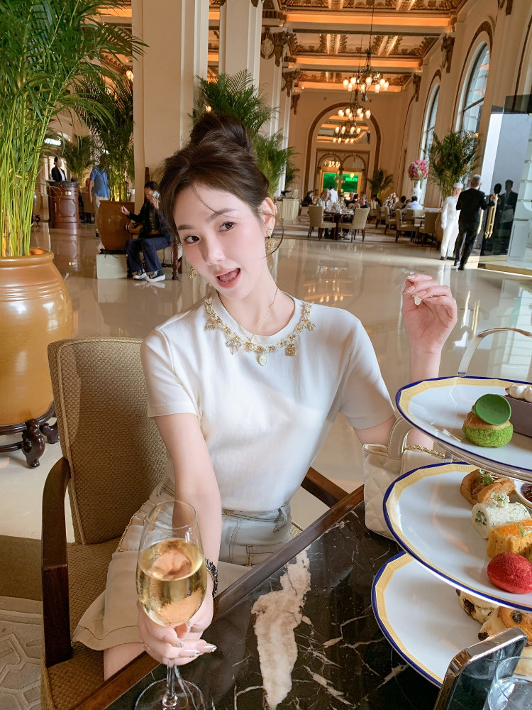 Woman wearing a white short-sleeve top and light skirt in a luxury restaurant setting