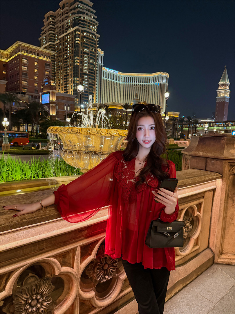 Woman wearing a red sheer lace top and black pants at night with a black handbag